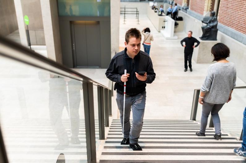 Man met geleidestok op trap in museum
