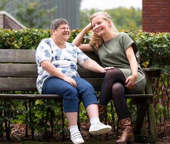 Bewoner en client zitten buiten te lachen op een bankje