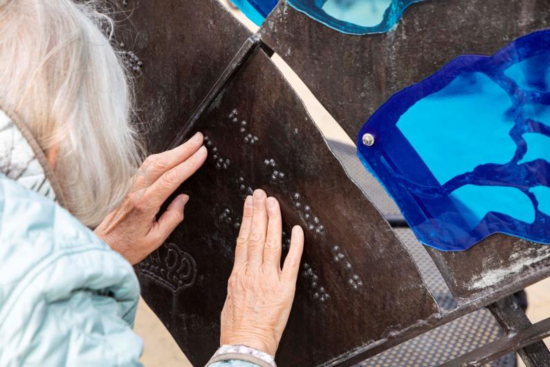 Oudere dame voelt braille op bankje